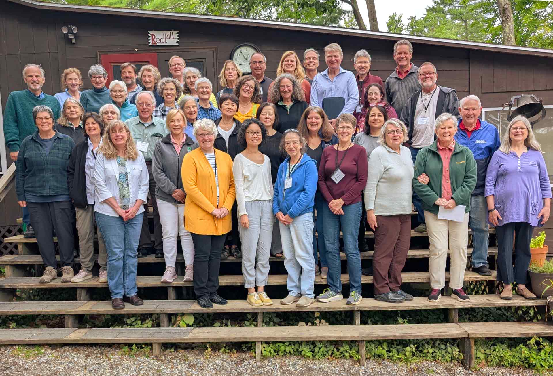Adult Programs A large group of adults, both men and women, stand together smiling on outdoor wooden steps in front of a dark building, celebrating their participation in Adult Programs.