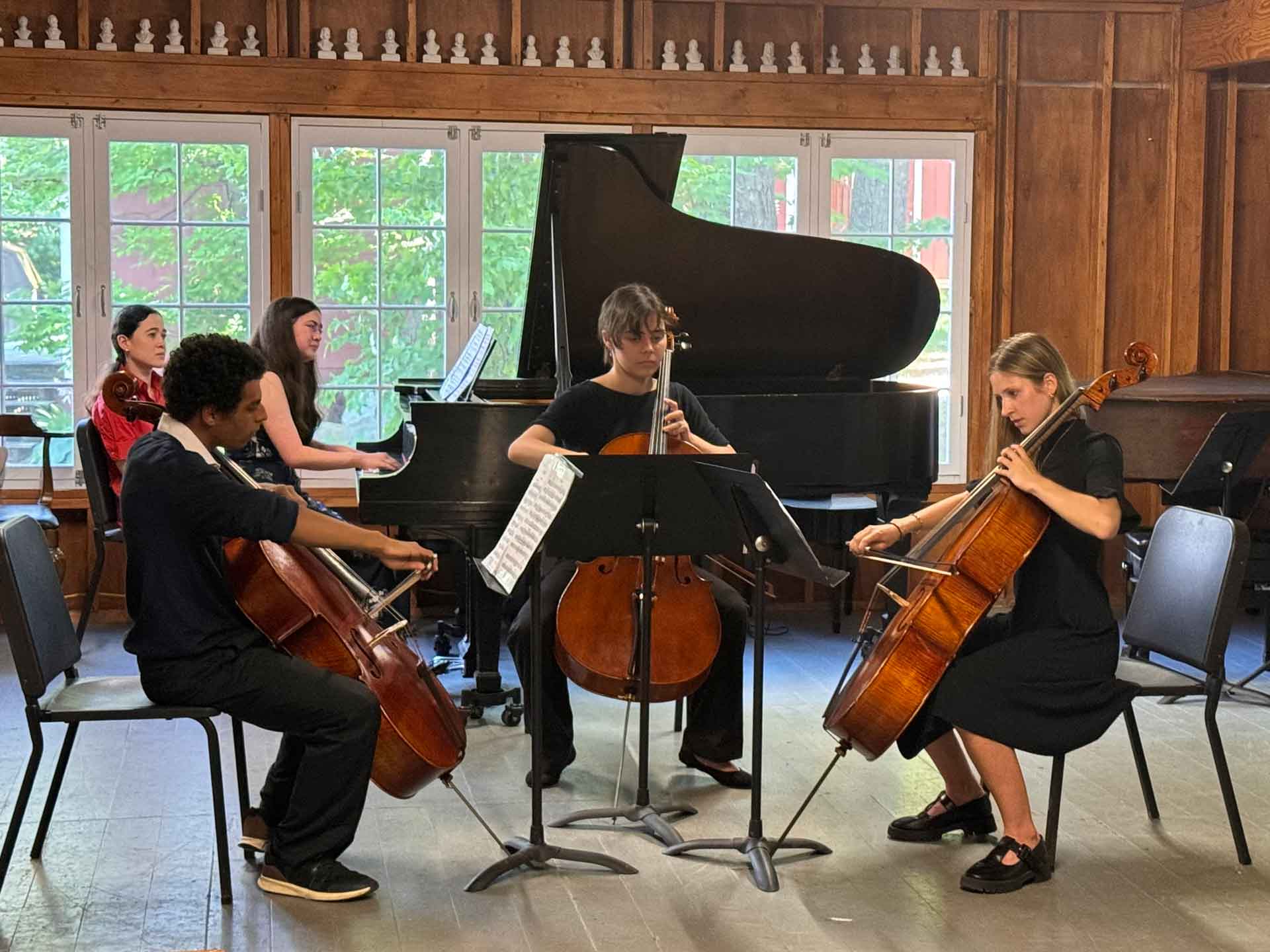 Youth Programs Four musicians perform indoors with cello, violin, and piano; sheet music stands in front, and a grand piano is in the background by large windows—a perfect setting for engaging youth programs or music-themed teen activities.