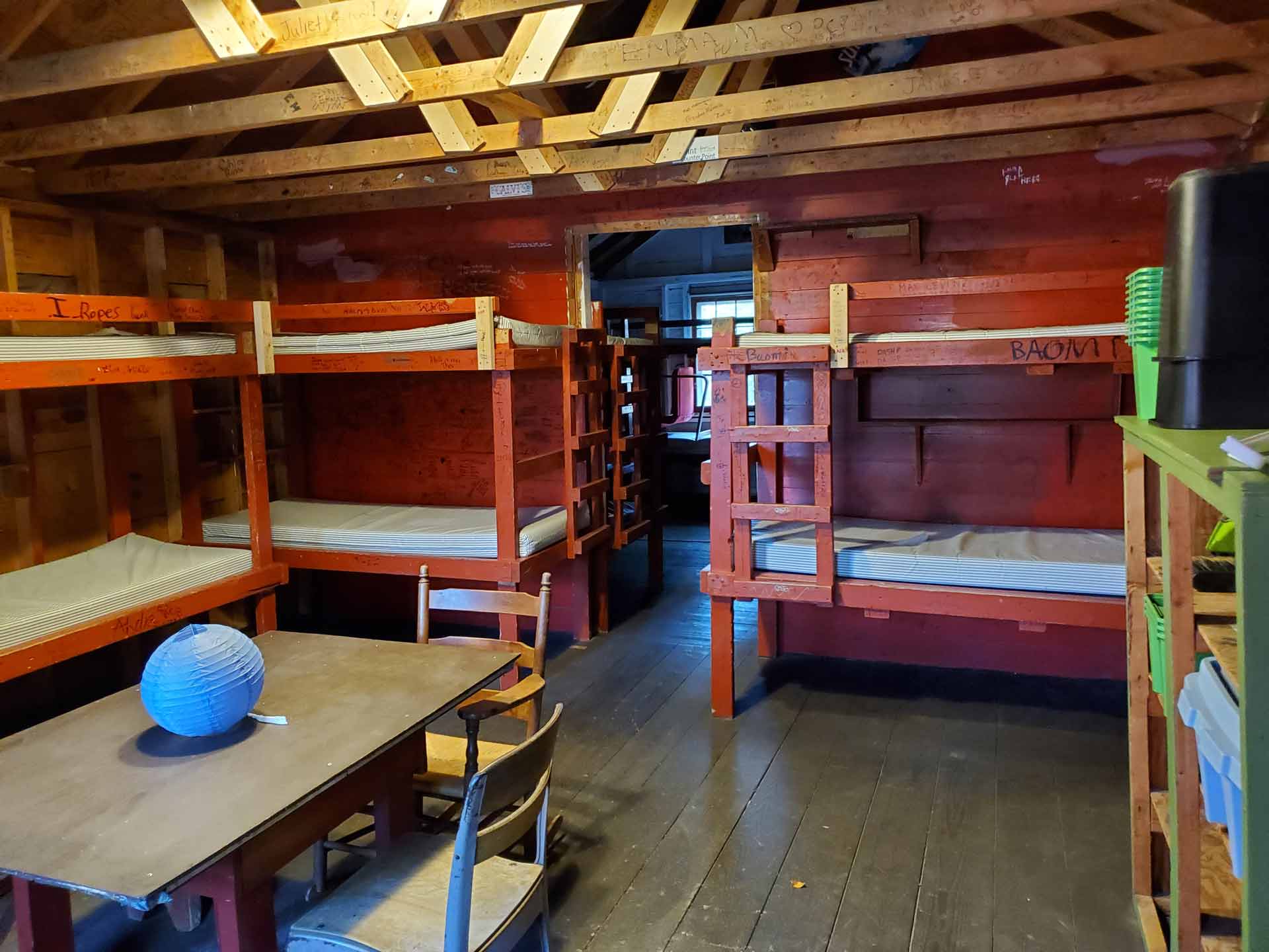 About Point CounterPoint A wooden cabin room at Point CounterPoint with four bunk beds, a table with chairs, and exposed ceiling beams. Mattresses are bare, and a blue paper lantern sits on the table.